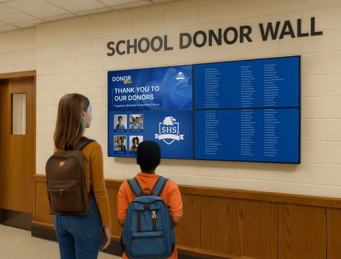 2 students standing in front of a school's digital donor wall display
