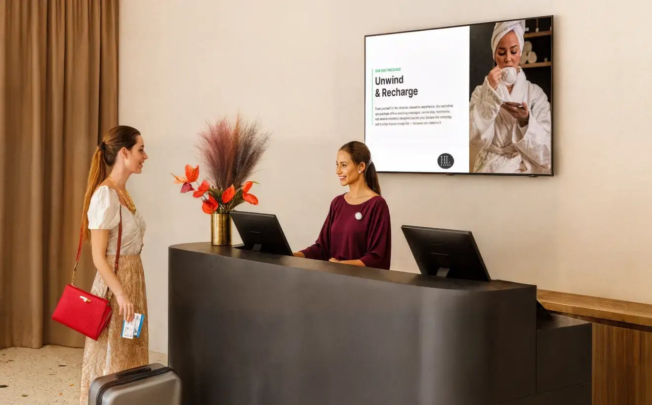 A female customer speaking with the receptionist of a spa facing a large display signage on the wall