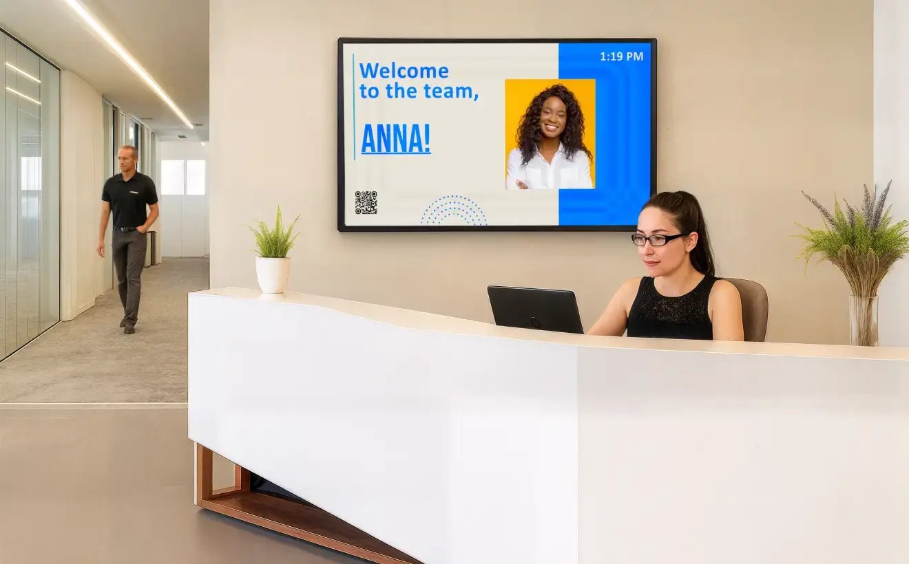 An office receptionist at her desk with a large digital signage display in the background