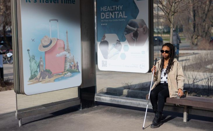 A woman sitting on a bus stop with digital signage screens behind her.