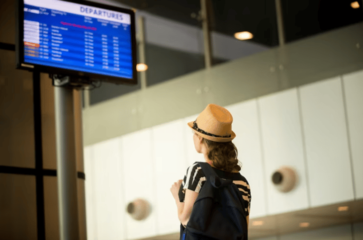 A woman referring to an airport digital sign for departure information.