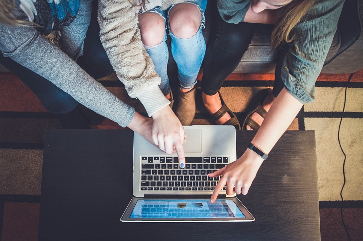 3 students in a classroom sitting in front of a laptop pointing.