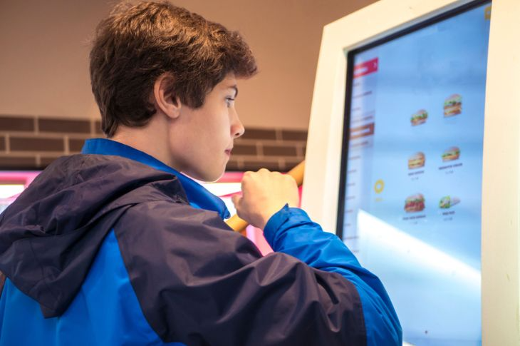 A young man looking at the menu through a digital signage screen.