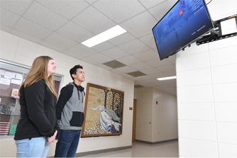 two students looking up at digital signage in school hallway