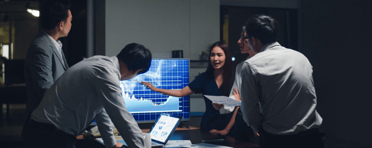 Employees having a meeting with company data on a digital screen.