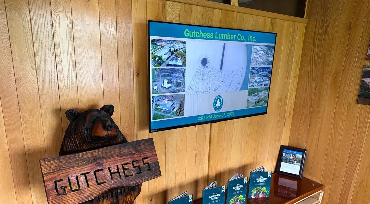 Rise Vision display showing Gutchess Lumber Co. content in a wood-paneled lobby