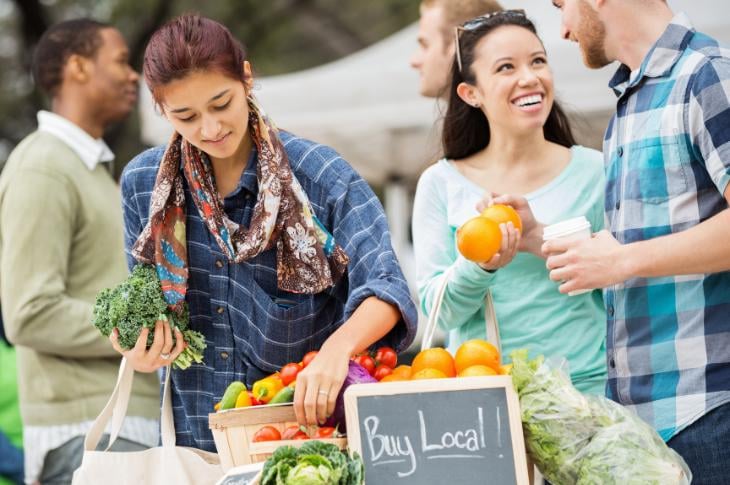 Grocers holding their produce and a buy local sign.