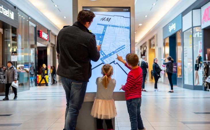 A father with his two kids using Location-based services (LBS) that are part of a mall directory digital signage display.