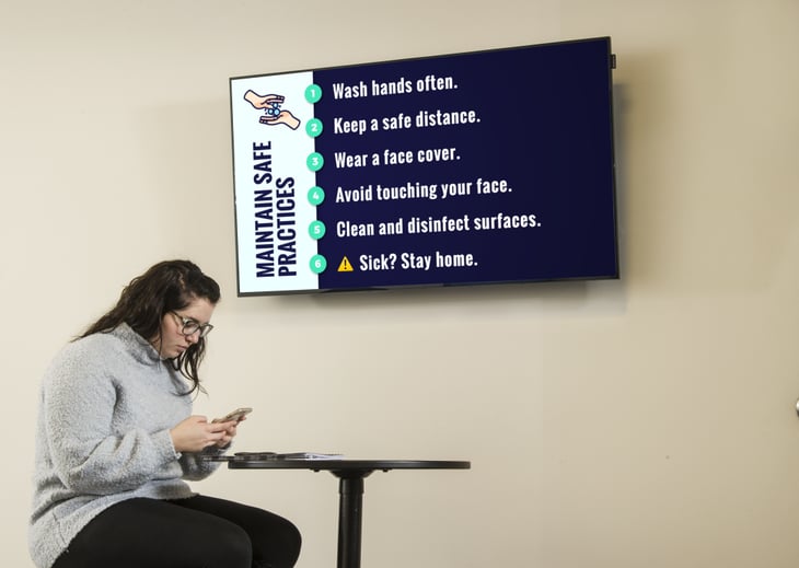 A girl sitting in front of a digital sign explaining safety best practices