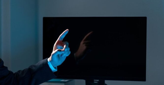 Man pointing a finger upward in front of a monitor.