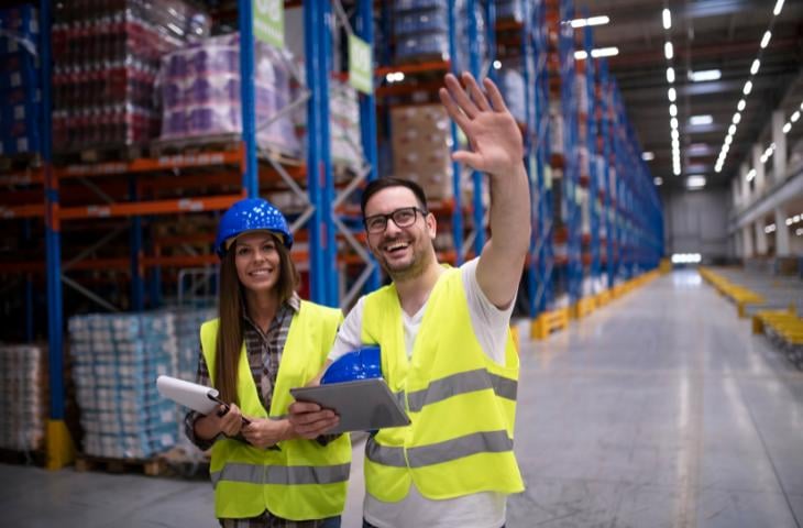 Happy warehouse employees with their right arms held up.