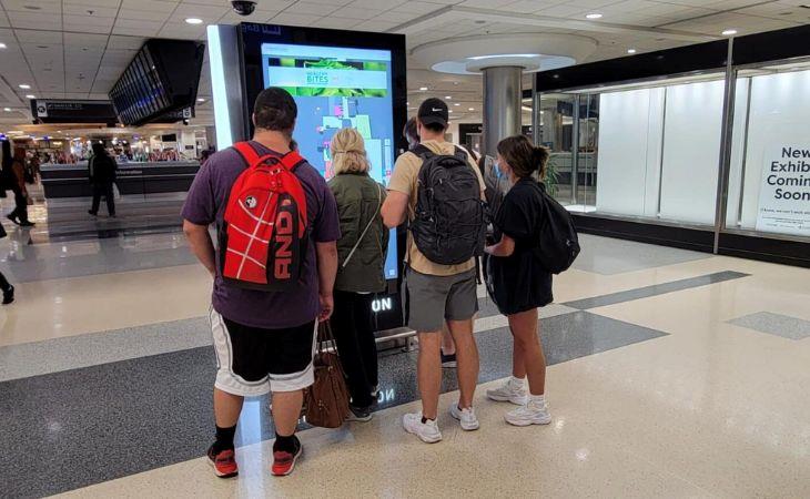 A group of travelers using a digital directory in an airport for wayfinding assistance.