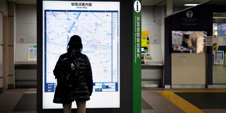 A woman is looking at a digital board for wayfinding assistance.