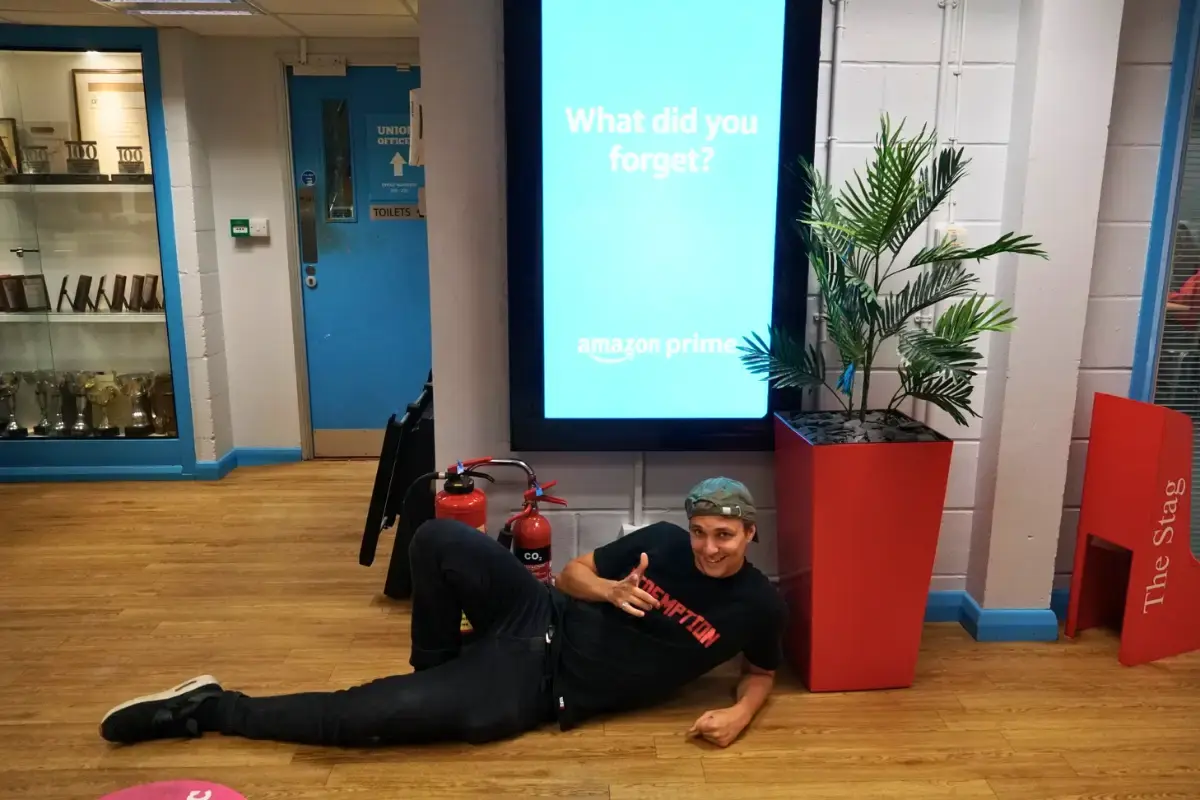 A male lying ont he floor next to a large digital signage poster