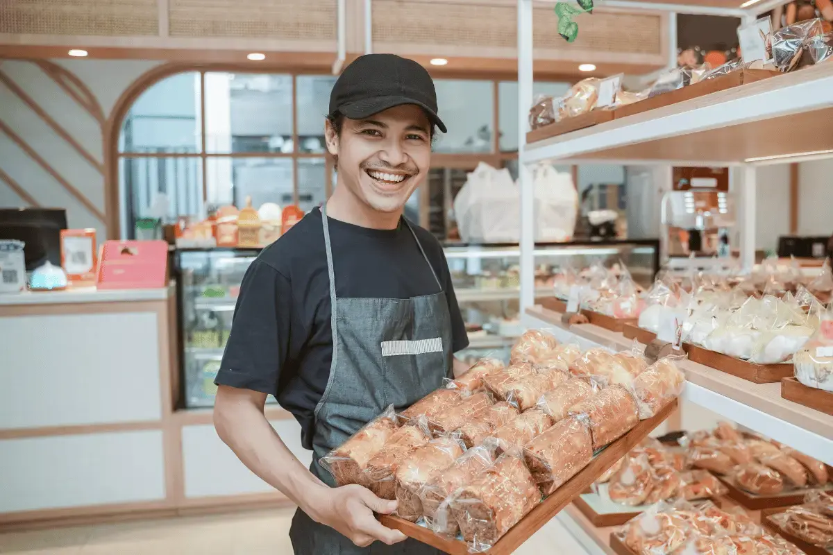 Grocery store clerk holding a large pan with pastries and bread