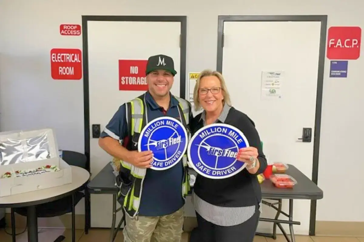 A male and feamle warehouse worker and driver holding million mile safe driver signs
