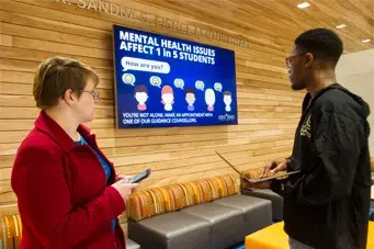 Male and female student viewing a digital signage display about mental health