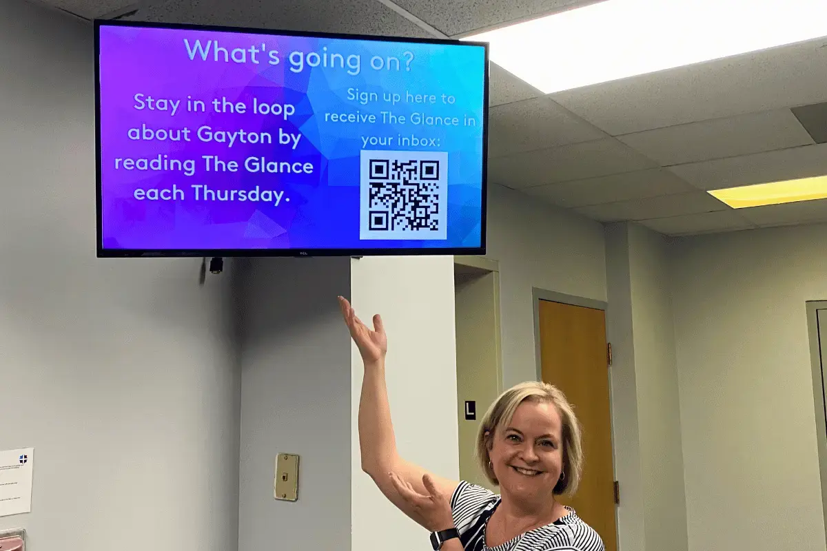 A female staff member in a senior livings facility pointing to the digital signage mounted on the wall