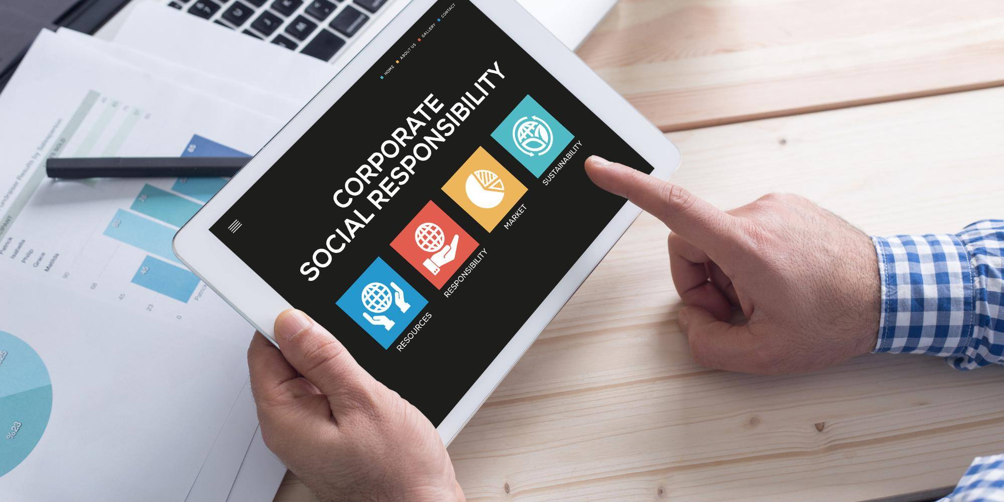 A man holding a finger on the tablet that says corporate social responsibility.