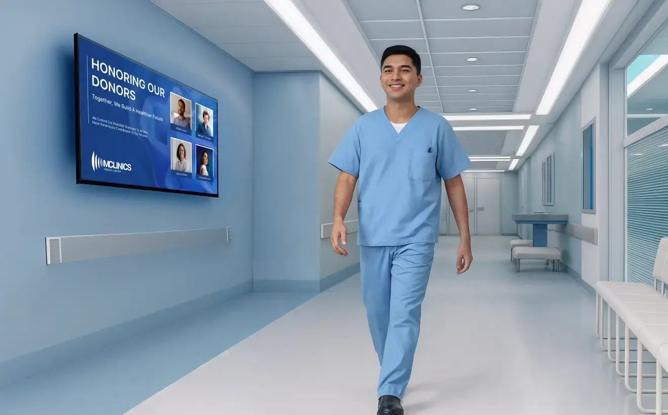 A medical practitioner walking through a hospital hallway with a digital donor board mounted on the wall
