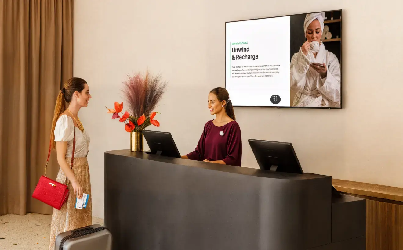 A female customer speaking with the receptionist of a spa facing a large display signage on the wall