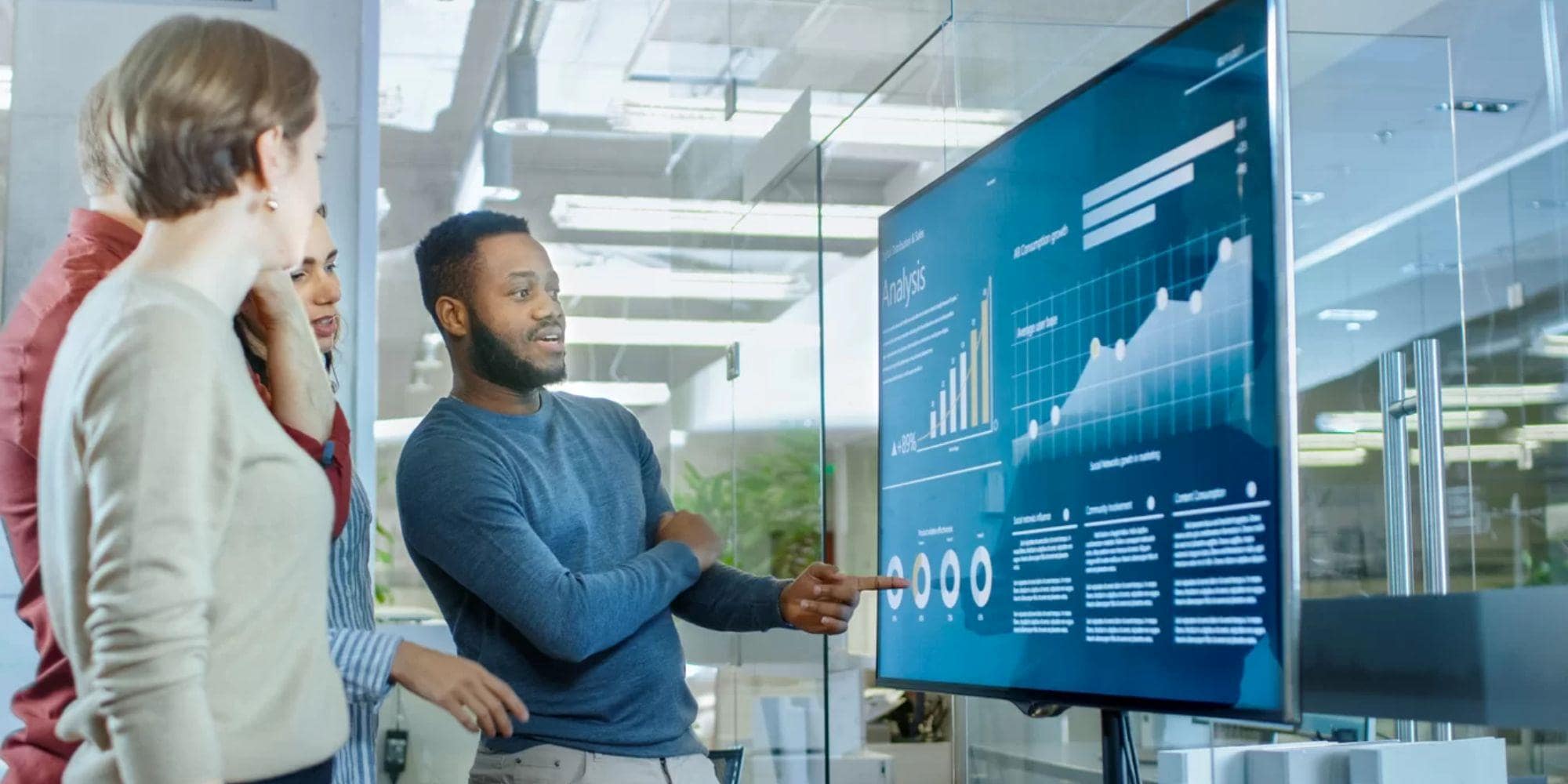 A team of analysts using data displayed on a digital signage screen for quality management insight for improving a manufacturing business.