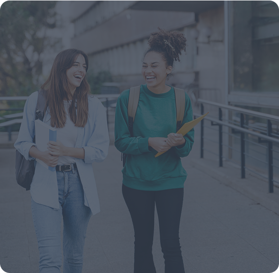 Two young women walking and laughing in the walkway of a university or college