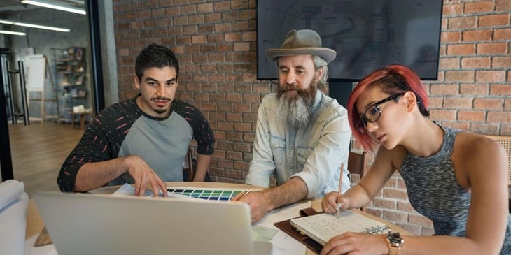 Two men and one woman collaborate in a modern workplace setting, illustrating effective ways to communicate with millennials in the workplace.