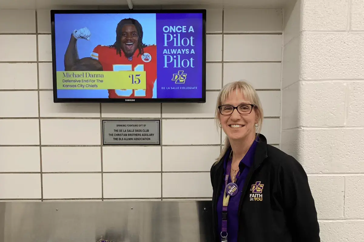 A female teacher in front of digital signage in a school hallway