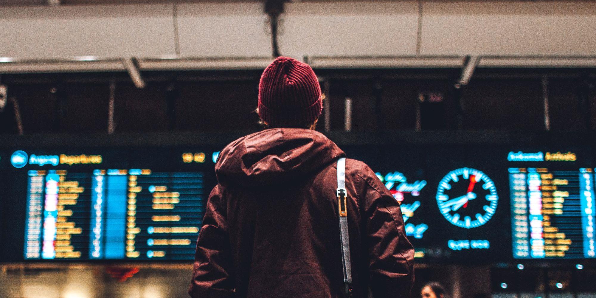 Man standing at the train station and looking at the digital timetable.